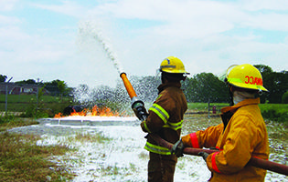 Two Fire Science students holding a hose pointed towards a fire