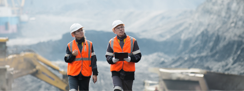 Two People in Construction Outfits Walking Around a Site in the Mountains